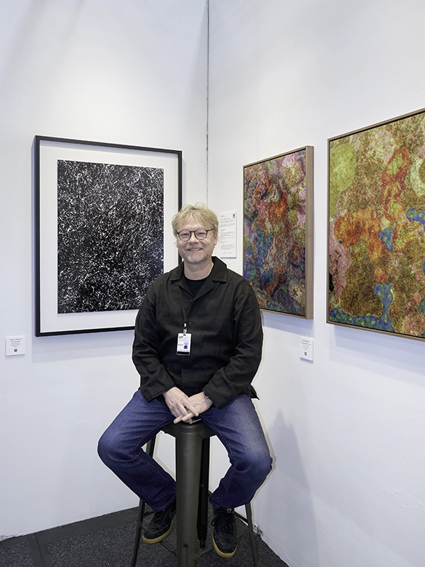 Alexej Sachov seated in his booth at Artexpo New York 2026, with works from The Secret Code of Nature and The Jewel of Nature series